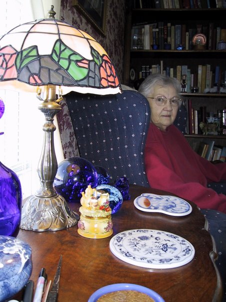 Mom in her blue chair, surrounded by blue and white glass, and her books.